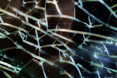 Spiderweb of cracks in glass against a dark background, representing the complex impact of domestic violence against men.