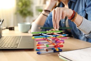 A woman fidgets by balancing a pencil on a stack of pens next to an open laptop, representing ADHD in adults.