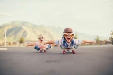 Two children wearing aviator goggles and hats glide on skateboards with arms outstretched, illustrating ADHD in children.