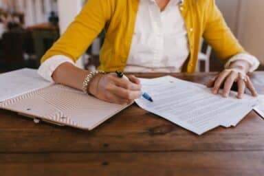 Close-up of a person in a yellow cardigan reviewing and signing legal documents for advance health care directives.