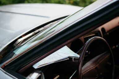 A paper map rests on the dashboard of a car near the steering wheel, representing the challenges and adjustments of how aging affects driving.