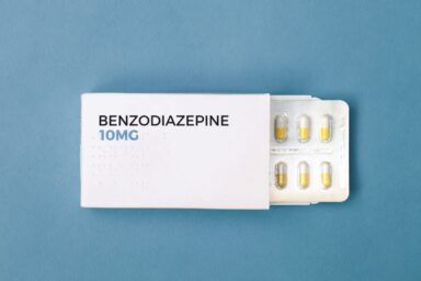 A white box of Benzodiazepine 10mg sits on a light blue background with several yellow capsules visible, representing anti-anxiety medication.