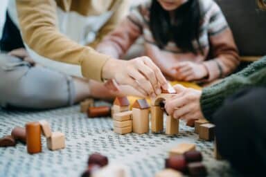Close-up of hands and a child building a structure with wooden toy blocks during a therapy session.