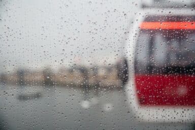 A glimpse of a train moving past, framed by a rain-soaked window, illustrating the journey and the surrounding environment.