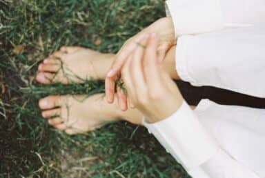 Barefoot person sitting on green grass in white clothing, practicing mindfulness and grounding.
