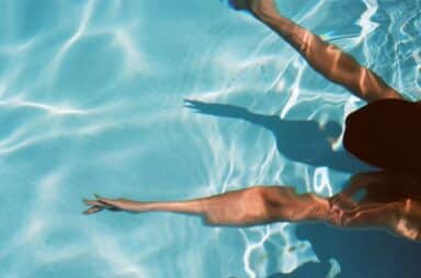 A person swims through clear blue water, their arms extended forward in a pool.