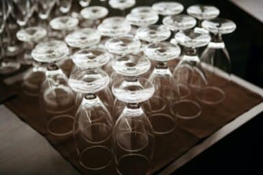 An image shows dozens of empty wine glasses turned upside down on a dark brown surface.
