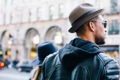 A man in a fedora, sunglasses, and leather jacket walks through a bustling city street, representing the journey of bipolar disorder treatment.