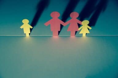 Four paper cutouts of a family—two pink adults and two yellow children—stand on a blue surface, representing blended families.