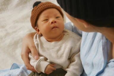 A close-up of a person cradling a newborn baby wearing a brown knit hat, illustrating the blessings of new babies.
