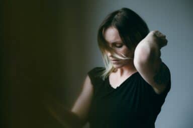 A woman with blonde-streaked hair wearing a black shirt looks down with a hand to her head, representing bulimia nervosa.
