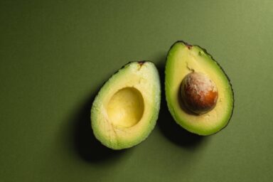 An avocado sliced in half with the pit still in one side, resting on a dark green surface, representing choosing healthy fats.