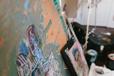 Vibrant, abstract mixed-media paintings and sketches lean against a wall in an artist's studio space.