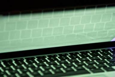 A keyboard's reflection is visible on a laptop screen that is partially closed.