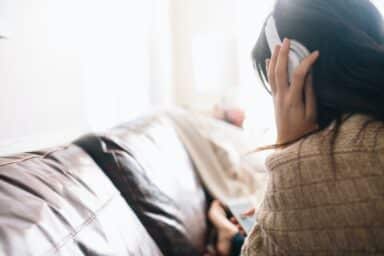 A young person with long dark hair sits on a sofa wearing white headphones and looking out a bright window, representing a teenager's guide to depression.