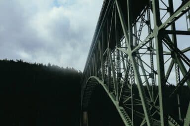 Low-angle shot looking up at the intricate steel girders of a large bridge against a cloudy sky, representing living with dementia.