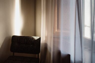 A chair positioned in front of a window adorned with elegant curtains, creating a morose atmosphere suggesting depression symptoms.