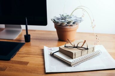 A desk featuring a laptop, an open book, and a small potted plant, creating a cozy workspace atmosphere.