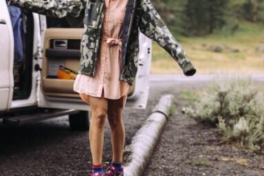 A person wearing a pink dress and a camouflage jacket balances on a fallen log outdoors, representing eating disorder recovery.