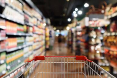 A red shopping cart pushed down a blurred grocery store aisle filled with stocked shelves.