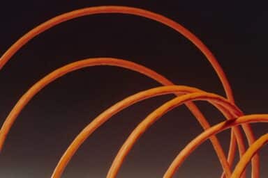 Four orange cables curve in overlapping arches against a dark, shadowy background.