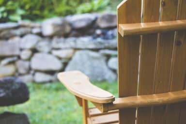 Empty wooden Adirondack chair facing a blurred stone wall and garden, evoking the solitude associated with elder abuse.