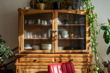 A wooden cabinet beside a chair, adorned with various green plants, creating a cozy and inviting atmosphere.