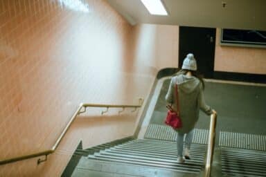 Woman in a grey hoodie and beanie walks down a subway staircase, signifying the journey of getting out of an abusive relationship.