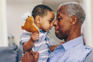 Older adult and young child facing one another with the child holding a small brown stuffed animal