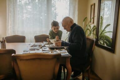 An older man and young boy sitting at a table looking at old photographs, depicting grandparents raising grandchildren.