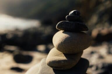 A stack of smooth stones forms a small cairn on a sunny beach, representing helping someone with BPD.