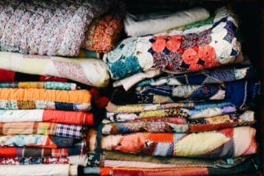 Stacks of colorful handmade quilts and textured blankets folded and piled high