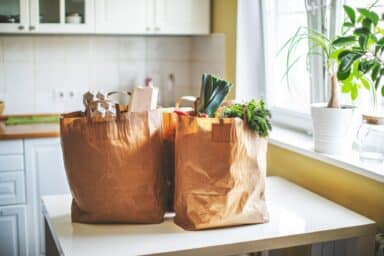 Two brown paper grocery bags filled with fresh produce and eggs sit on a white kitchen counter.