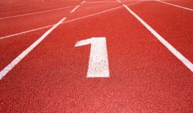 White number one painted on a red running track at the starting line of a race.