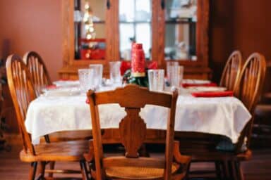 A festive holiday dining table with a white tablecloth, red napkins, and crystal glasses in a cozy room.