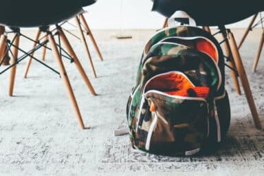 A lone backpack rests on the floor beside a row of empty chairs in a spacious classroom, symbolizing the challenges of learning disabilities.