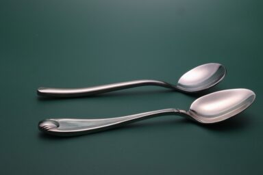 Two silver spoons with curved handles lie parallel on a dark green surface, representing living well with a disability.