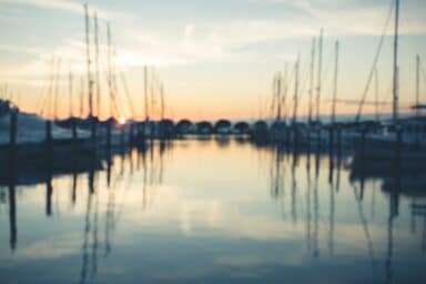 Blurred view of a harbor with numerous sailboats and calm water at sunset.
