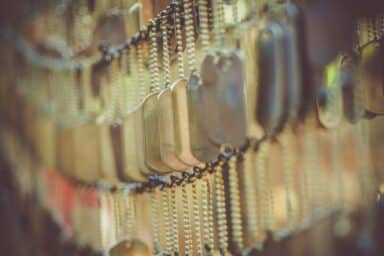 Rows of military dog tags hanging from metal chains with a shallow depth of field and soft, blurred background.