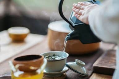 Person pours hot water from a black teapot into a cup with tea leaves for quick stress relief.