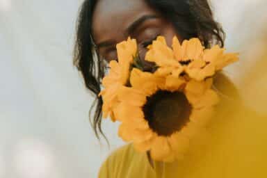 Close-up of a woman with closed eyes holding vibrant yellow sunflowers that partially cover her face.