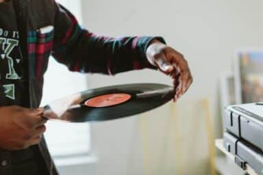 A person in a colorful plaid shirt carefully holds a vinyl record, preparing to place it on a turntable.
