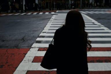 A woman stands on a city crosswalk, surrounded by urban buildings and bustling streets.