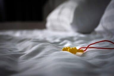Yellow earplugs with a red cord rest on rumpled white bedsheets