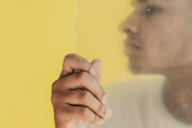 A person's profile is seen through a frosted glass pane with their hand resting on the surface, representing social anxiety disorder.