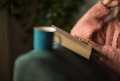 A person in a pink sweater sits with a book and a blue mug, illustrating simple ways to relax and recharge.