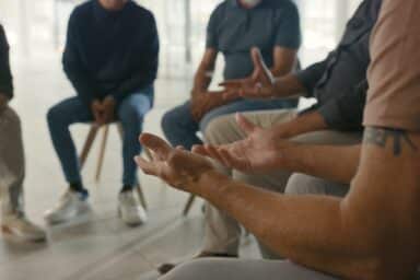 A group of people sitting in a circle, focusing on a man gesturing with open hands during a support group session.