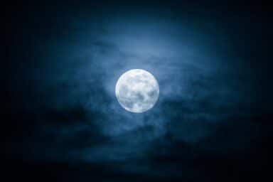 Full moon glows brightly against a dark, cloudy night sky, illustrating nighttime and the sleep cycle.