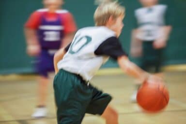 A blurred action shot of a young boy in a sports jersey dribbling a basketball on a court, representing active treatment for child ADHD.