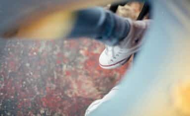 A person's foot wearing a white canvas sneaker and denim jeans, seen through a blurred foreground lens flare.
